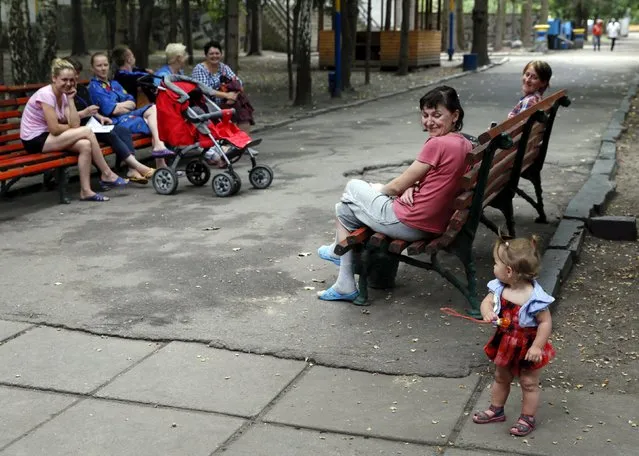 Adults look at a girl as they sit on benches in the compound of a health and rest centre which serves as a temporary accommodation for refugees from eastern regions of the country in the town of Korostyshiv, Zhytomyr region, Ukraine, July 30, 2015. (Photo by Valentyn Ogirenko/Reuters)