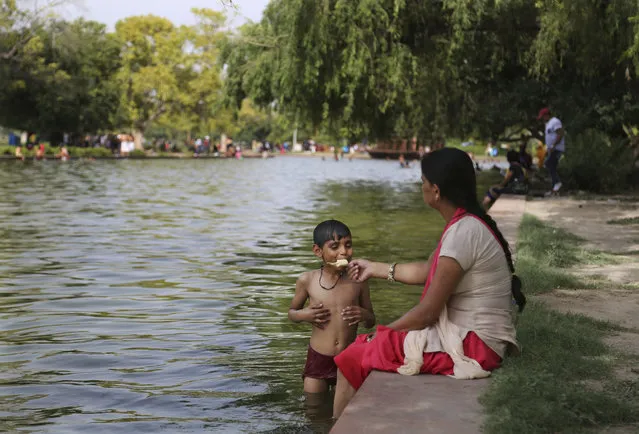 An Indian woman offers an ice-cream to her son as he cools off in a pond near the India Gate monument on a hot day in New Delhi, India, Tuesday, June 6, 2017. (Photo by Altaf Qadri/AP Photo)