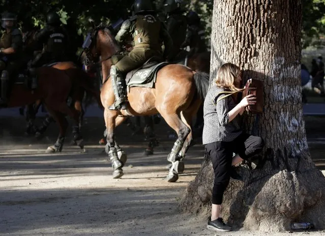 A woman takes cover behind a tree during clashes between riot police officers and demonstrators at a protest against Chile's government in Santiago, Chile on December 18, 2019. (Photo by Andres Martinez Casares/Reuters)