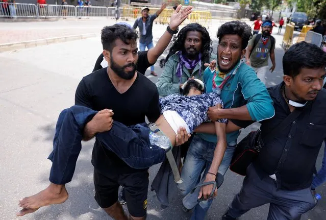 Demonstrators carry an injured person during a clash in front of Sri Lankan Prime Minister Ranil Wickremasinghe's office at a protest demanding for his resignation, after President Gotabaya Rajapaksa fled, amid the country's economic crisis, in Colombo, Sri Lanka, July 13, 2022. (Photo by Dinuka Liyanawatte/Reuters)