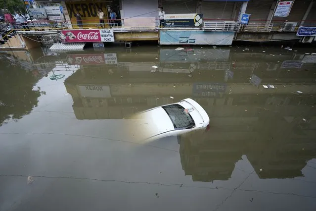 A car is seen submerged at a water logged shopping complex after heavy rain lashed city on Sunday night in Ahmedabad, India, Monday, July 11, 2022. India's annual monsoon season runs from June to September. (Photo by Ajit Solanki/AP Photo)