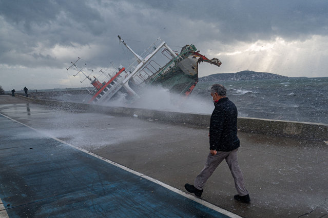 A man walks near a boat which has capsized due to strong winds in Istanbul on November 30, 2021. Strong winds continue to blow across Istanbul where the Bosphorus strait is temporarily closed to boat traffic. Four people were killed and dozens injured on Monday in Istanbul, which was hit by high winds. (Photo by Yasin Akgul/AFP Photo)