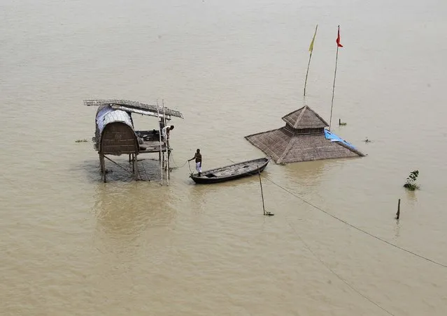 A sadhu or Hindu holy man stands on a boat near a submerged hut on the flooded banks of river Ganga after heavy monsoon rains in the northern Indian city of Allahabad August 9, 2014. The outlook for the second half of India's four-month monsoon has improved after some above-average rainfall that is also expected to spill over into next week, weather experts said on August 7. (Photo by Jitendra Prakash/Reuters)