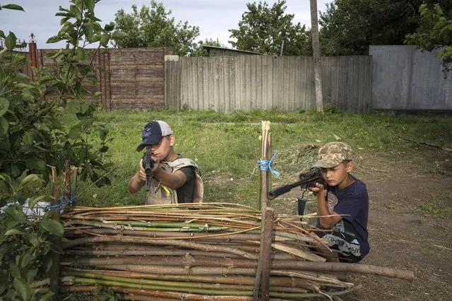 Maksym and Andrii, 11 years old boys, play with plastic guns at a self-made checkpoint on the highway in Kharkiv region, Ukraine, Wednesday, July 20, 2022. (Photo by Evgeniy Maloletka/AP Photo)