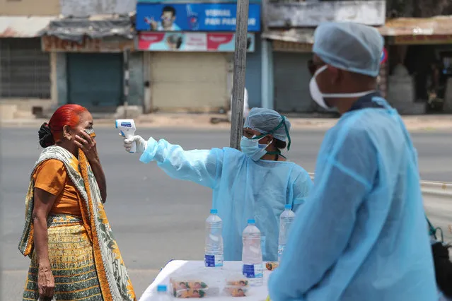 In this April 8, 2020 file photo, an Indian health worker checks the temperature of a woman during lockdown to prevent the spread of new coronavirus in Ahmedabad, India. India, a bustling country of 1.3 billion people, has slowed to an uncharacteristic crawl, transforming ordinary scenes of daily life into a surreal landscape. The country is now under what has been described as the world’s biggest lockdown, aimed at keeping the coronavirus from spreading and overwhelming the country’s enfeebled health care system. (Photo by Ajit Solanki/AP Photo/File)