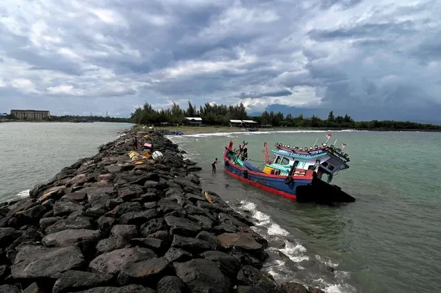 A fisherman secures his boat that got caught in bad weather, at a beach in Banda Aceh on August 24, 2022. (Photo by Chaideer Mahyuddin/AFP Photo)