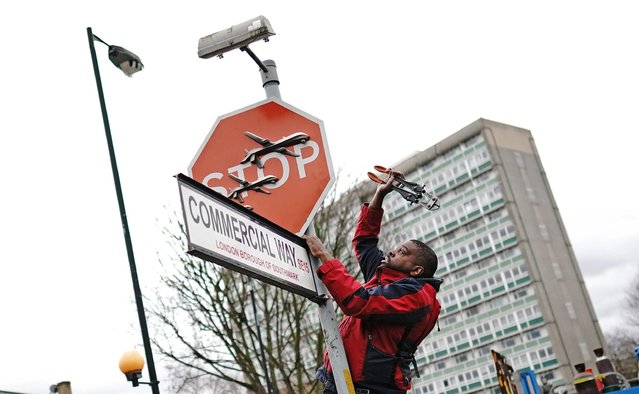 A person removes a piece of art work by Banksy, which shows what looks like three drones on a traffic stop sign, which was unveiled at the intersection of Southampton Way and Commercial Way in Peckham, south east London, Friday December 22, 2023. (Photo by Aaron Chown/PA Wire via AP Photo)