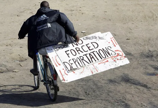 A migrant holds a placard which reads “No Forced Deportations” as he rides his bicycle at the makeshift camp called “The New Jungle” in Calais, France, September 18, 2015. (Photo by Regis Duvignau/Reuters)
