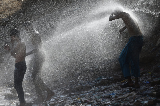 Residents cool off as water sprays from a water pipeline during a hot summer day at a slum area in Karachi on July 2, 2020. (Photo by Asif Hassan/AFP Photo)