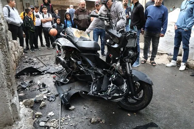 People look at a damaged motorcycle following an explosion that killed a Palestinian man in the old city of Nablus, 23 October 2022. Tamer Kilani, a senior member of Palestinian armed group Lion's Den, was killed in the explosion on 23 October. (Photo by Alaa Badarneh/EPA/EFE)