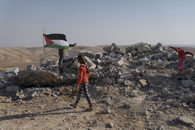 Palestinians stand on the remains of a school with a Palestinian flag after it was demolished by the Israeli military, in the occupied West Bank village of Masafer Yatta, Wednesday, November 23, 2022. The Israeli military demolished the school on Wednesday following a court ruling earlier this year that upheld a long-standing expulsion order against eight Palestinian hamlets in the area. (Photo by Mahmoud Illean/AP Photo)