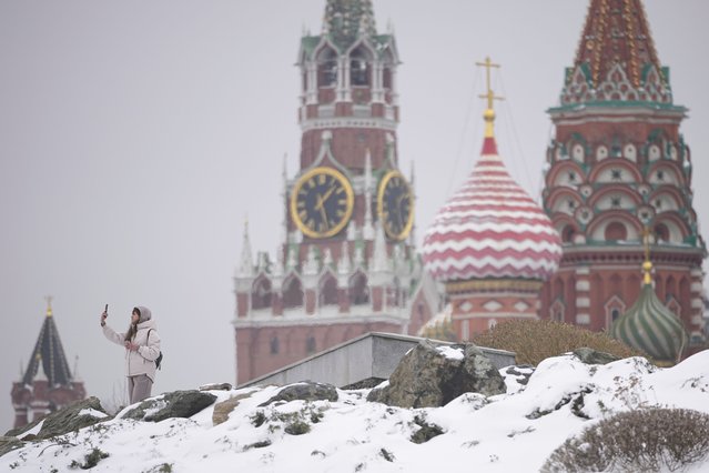 A woman takes selfies at the Zaryadye park, with the Spasskaya tower of the Kremlin and St. Basil's Cathedral in the background, after a snowfall in Moscow, Monday, April 7, 2025. (Photo by Pavel Bednyakov/AP Photo)