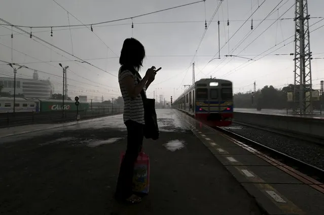 A woman uses her mobile phone as she waits for a train during a rainy day at a train station in Jakarta, Indonesia, May 4, 2015.    REUTERS/Beawiharta 