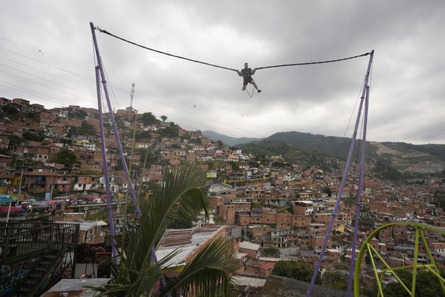 A tourist rides a bungee jump in the Comuna 13 neighborhood of Medellin, Colombia, Friday, February 2, 2024. Once a battleground for fighting among drug cartels, leftist guerrillas, military forces, and government-linked paramilitary groups, the area is now a tourist attraction. (Photo by Fernando Vergara/AP Photo)