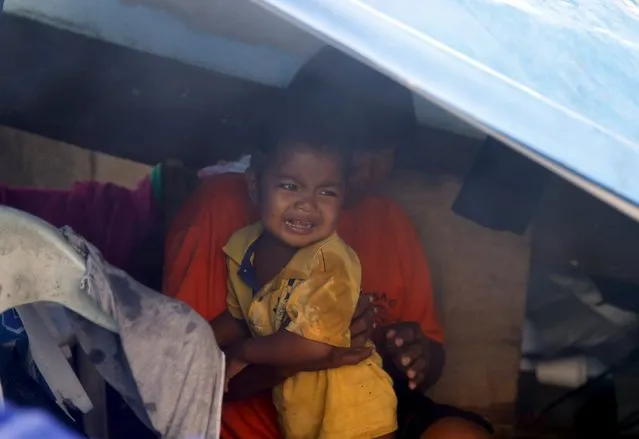 A child cries inside a temporary shelter with his mother under their boat that was put up in baywalk due to Typhoon Koppu in Manila, October 18, 2015. (Photo by Erik De Castro/Reuters)