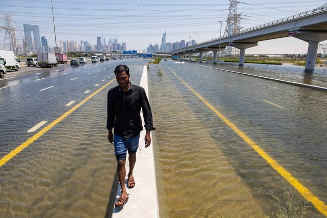 A man walks along a road barrier among floodwater caused by heavy rain on Sheikh Zayed Road highway in Dubai, United Arab Emirates, Thursday, April 18, 2024. The United Arab Emirates attempted to dry out Thursday from the heaviest rain the desert nation has ever recorded, a deluge that flooded out Dubai International Airport and disrupted flights through the world's busiest airfield for international travel. (Photo by Christopher Pike/AP Photo)