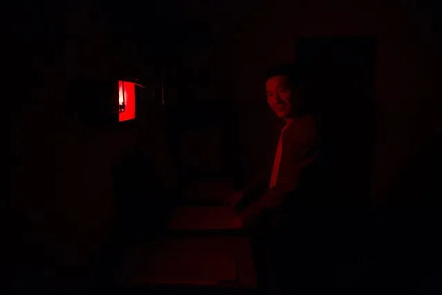 Yang Yang, an x-ray technician, poses for a photograph under the red light in his lab in the radiology department of Yangjia Hospital in Wuyi County, Zhejiang Province, China October 19, 2015. Behind the vine-covered walls and broken windows of the radiology department, a single staff member and a single X-ray machine serve the few remaining pneumoconiosis patients at Yangjia Hospital. (Photo by Damir Sagolj/Reuters)