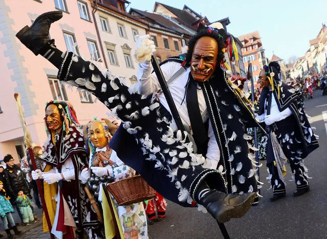 A carnival reveller wearing a carved wooden mask and a “Federhannes” (“Feather Hannes”) costume jumps during the traditional folklore procession “Narrensprung” (“Fools Jump”) dating back to the 14th century as part of the Swabian-Alemannic Rose Monday celebrations in the Black Forest town of Rottweil, Germany on February 20, 2023. (Photo by Wolfgang Rattay/Reuters)