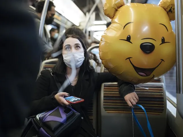 A masked woman holds a Winnie the Pooh inflatable balloon, inside the subway, in Paris, Thursday October 29, 2020. Some doctors expressed relief but business owners despaired as France prepared to shut down again for a month to try to put the brakes on the fast-moving virus. (Photo by Lewis Joly/AP Photo)