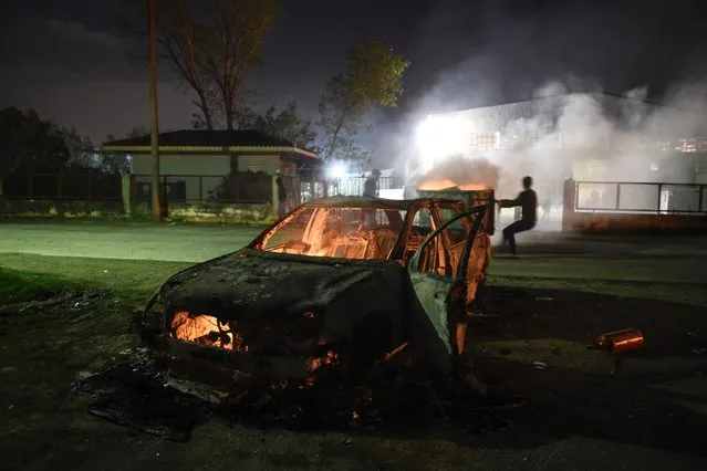 Migrants pull a garbage can behind the remains of a burnt car outside the refugee camp of Oreokastro, near the northern Greek town of Thessaloniki, on October 16, 2016. Migrants living in the camp rioted Sunday night after a woman and her son were struck and killed by a car outside the camp, police report. (Photo by Giannis Papanikos/AP Photo)