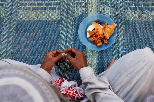 A man holds tasbih, or prayer beads, as he sits with a plate of food before breaking fast during the fasting month of Ramadan, at a roadside in Karachi, Pakistan on March 28, 2023. (Photo by Akhtar Soomro/Reuters)