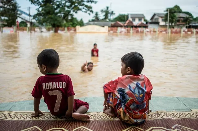 Two boys look on as their friends play in floodwaters in Pengkalan Chepa, near Kota Bharu on December 27, 2014. (Photo by Mohd Rasfan/AFP Photo)