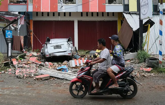Motorist ride past the wreckage of a car damaged in an earthquake in Mamuju, West Sulawesi, Indonesia, Friday, January 15, 2021. A strong, shallow earthquake shook Indonesia's Sulawesi island just after midnight, causing landslides and sending people fleeing from their homes in the nighttime darkness. (Photo by Sadly Ashari Said/AP Photo)