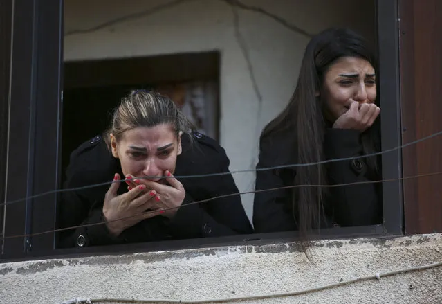 Two Alawite women mourn as they look from a window during the funeral procession of those who were killed in an overnight suicide bombing at a coffee shop in the northern port city of Tripoli, Lebanon, Sunday, January 11, 2015. (Photo by Hussein Malla/AP Photo)