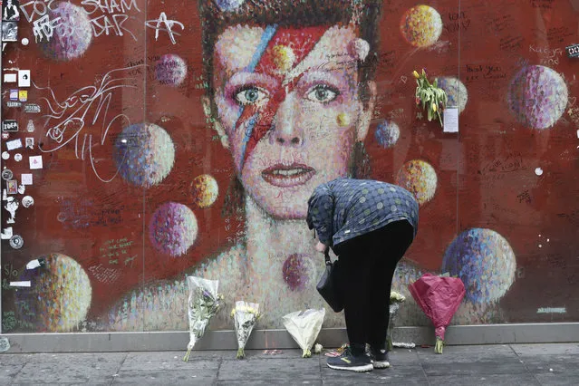 A woman lays a floral tribute at the David Bowie mural in Brixton, south London on the fifth anniversary of the singer's death, Sunday January 10, 2021. The singer-songwriter Bowie died of liver cancer at his home in New York, USA, on 10 January 2016. (Photo by Jonathan Brady/PA Wire via AP Photo)