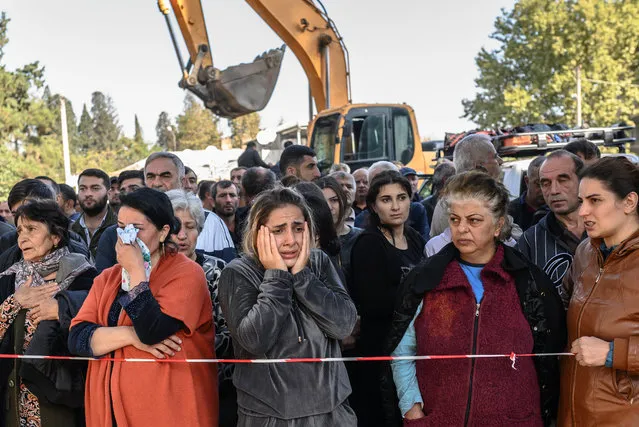 People stand behind caution tape as rescuers search for victims or survivors at the blast site hit by a rocket during the fighting between Armenia and Azerbaijan over the breakaway region of Nagorno-Karabakh, in the city of Ganja, Azerbaijan, on October 11, 2020. (Photo by Bulent Kilic/AFP Photo)