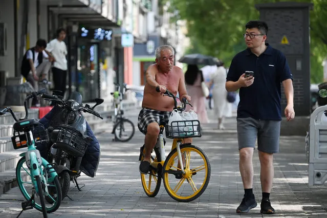 A shirtless man rides a bike during a heatwave in Beijing on June 23, 2023. (Photo by Greg Baker/AFP Photo)