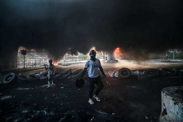 Protesters walk amidst smoke near a makeshift barricade during a crackdown by security forces on demonstrations against the military coup in Yangon on March 16, 2021. (Photo by AFP Photo/Stringer)