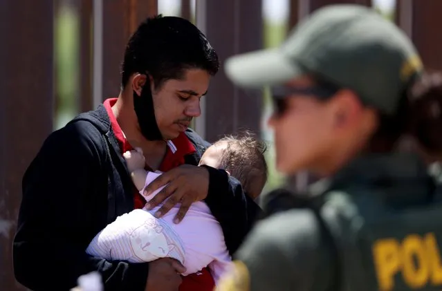 A man from Brazil holds his nine-month-old daughter as they wait to be transported by the U.S. Border Patrol after crossing into the United States from Mexico in Andrade, California, U.S., April 19, 2021. (Photo by Jim Urquhart/Reuters)