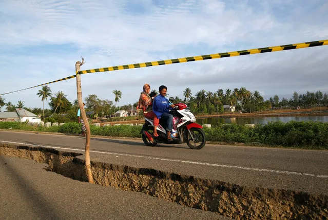A family drives their motorcycle past a section of road damaged following this week's strong earthquake in  Pidie Jaya, Aceh province, Indonesia, December 10, 2016. (Photo by Darren Whiteside/Reuters)