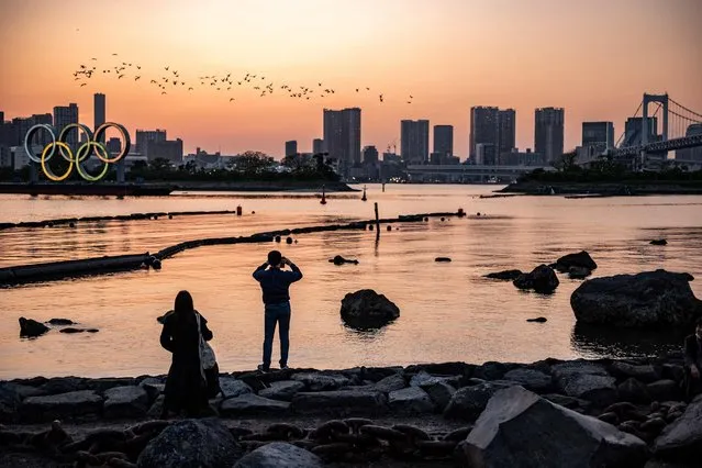 People take pictures as the Olympic rings are lit up at dusk on the Odaiba waterfront in Tokyo on July 22, 2021, on the eve of the start of the Tokyo 2020 Olympic Games. (Photo by Philip Fong/AFP Photo)