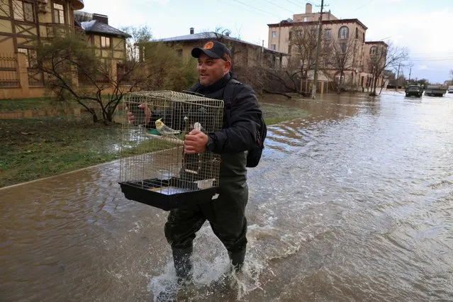 A man carries a cage with a parrot while walking along a flooded street following a storm in Yevpatoriya, Crimea on November 26, 2023. (Photo by Alexey Pavlishak/Reuters)