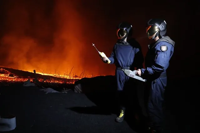 In this photo made available by Ume (Unidad Militar de Emergencias), Military Emergency Unit personal take gas reading measurements near a volcano on the Canary island of La Palma, Spain, in the early hours of Tuesday September 28, 2021. Lava flowing from an erupting volcano on the Spanish island of La Palma has picked up pace on its way to the sea. Officials say it is now within about 800 meters (875 yards) of the shoreline. When the molten rock eventually meets the sea water it could trigger explosions and toxic gas. (Photo by Luismi Ortiz/UME via AP Photo)