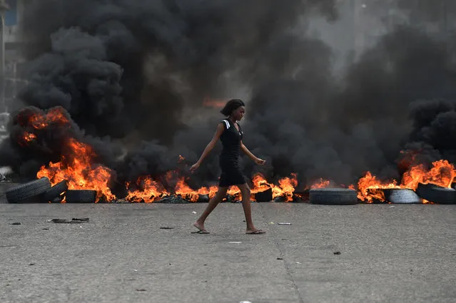 A woman walks past tire barricades set ablaze by demonstrators on the fourth day of protests in Port-au-Prince, February 10, 2019, against Haitian President Jovenel Moise and misue of Petrocaribe fund. (Photo by Héctor Retamal/AFP Photo)