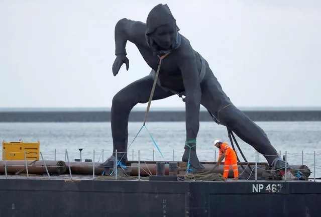 Britain's largest bronze sculpture, “Messenger” arrives by barge in Plymouth Sound before being taken by road to the Theatre Royal in Plymouth, Britain, March 18, 2019. The UK's largest bronze statue that shows a squatting woman has been pictured arriving on a barge – after being nicknamed “Radcliffe's Revenge”. The 23ft high sculpture of the crouching female figure is being put on display outside a theatre. Locals christened the creation – officially named Messenger – in honour of the athlete Paula Radcliffe after she stopped for a toilet break during the London Marathon. (Photo by Peter Nicholls/Reuters)