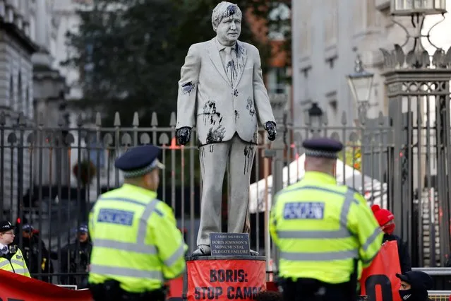 Police officers stand guard as Greenpeace activists stage a sit-in after installing an oil-splattered statue of British Prime Minister Boris Johnson by artist Hugo Farmer at Downing Street in London on October 11, 2021 during a protest against the Cambo oil field project in the Shetland Islands. (Photo by Tolga Akmen/AFP Photo)