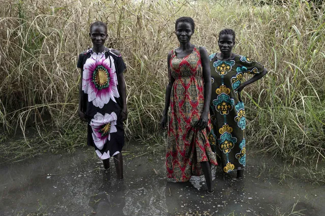 Three women pose for a portrait with their feet in the water, in Dijeri village, on the outskirts of Juba, South Sudan, Friday, October 1, 2021. Dijeri was flooded for a week when the waters receded at the end of September. It is the second year in a row that river Luri floods the village. Floods have displaced around 426,000 people across the country since May, according to the U.N humanitarian affairs office. (Photo by Adrienne Surprenant/AP Photo)