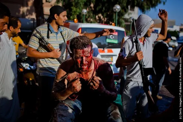 Libyan rebel fighters protect a pro-Gaddafi loyalist fighter from angry onlookers as he is brought in for medical attention to the Tripoli Central Hospital