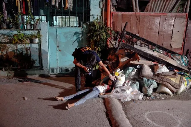 A policeman investigates at the site where a 17 year old girl and a 21 year old man were killed by unknown motorcycle-riding gunmen in an alley in Manila, Philippines early October 26, 2016. According to the police, a sign on a cardboard reading “Tulak ka, hayop ka”, which translates to “You are a (drug) pusher, you are an animal” was found with the the body of the killed man. (Photo by Damir Sagolj/Reuters)