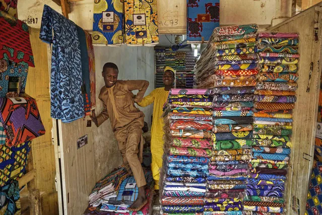 In this photo taken Tuesday, February 19, 2019, shopkeepers stand by stacks of the wax-printed fabric made in China that fills the market in Kano, northern Nigeria. The ancient dye pits of Kofar Mata in Kano were founded in 1498 and are said to be the last ones of their kind but some of their craftsmen grumble about competition from Chinese fabrics that have entered the markets and sell for half the price. (Photo by Ben Curtis/AP Photo)