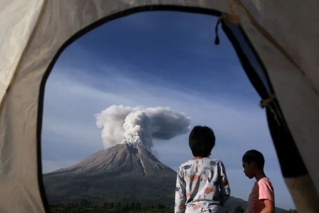 Campers are seen from the opening of a tent as they watch Mount Sinabung erupting in Karo, North Sumatra, Indonesia, Thursday, March 11, 2021. The 2,600-meter (8,530-feet) volcano unleashed an avalanche of searing gas clouds flowing down its slopes during eruption on Thursday. (Photo by Binsar Bakkara/AP Photo)