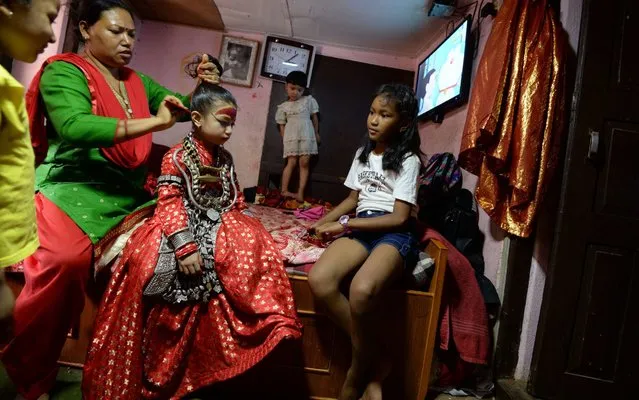 A relative combs the hairs of Nepal's Living Goddess, also called the “Kumari” (C), at her house in Patan in the outskirts of Kathmandu on June 9, 2019. The Kumari, considered a living goddess, attends festivities on the last day of the Rato Machindranath chariot festival, also known as Bhoto Jatra. The event is celebrated every year to herald good monsoon rains for increased rice harvest, prosperity and good luck and it is one of the main festivals observed by both the Buddhist and Hindu communities of Kathmandu. (Photo by Prakash Mathema/AFP Photo)