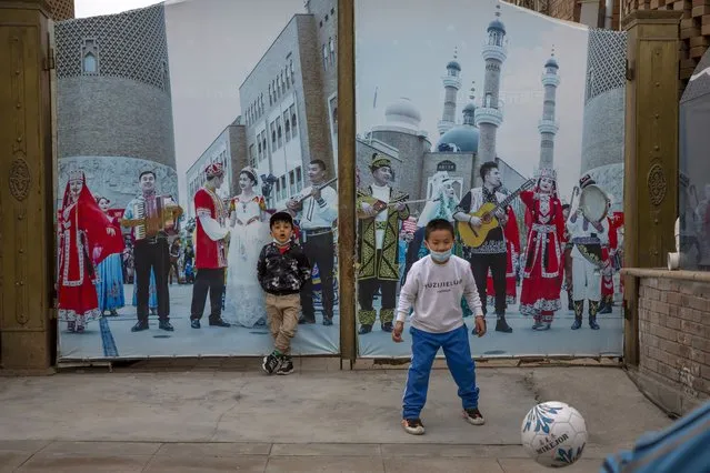 Children play soccer in front of a gate with a mural depicting Uyghur musicians at the International Grand Bazaar in Urumqi in western China's Xinjiang Uyghur Autonomous Region, as seen during a government organized trip for foreign journalists, April 21, 2021. As the Chinese government tightened its grip over its ethnic Uyghur population, it sentenced one man to death and three others to life in prison in 2021 for textbooks drawn in part from historical resistance movements that had once been sanctioned by the ruling Communist Party. (Photo by Mark Schiefelbein/AP Photo/File)