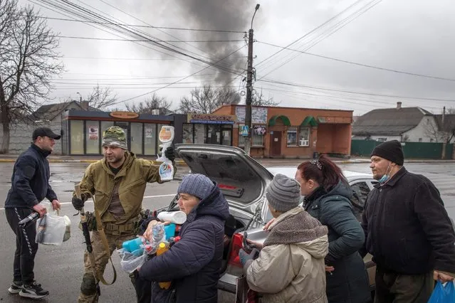 Residents crowd around to get food and other items handed out by members of the Ukrainian military as smoke rises from shelling on March 03, 2022 in Irpin, Ukraine. Russia continues assault on Ukraine's major cities, including the capital Kyiv, a week after launching a large-scale invasion of the country. (Photo by Chris McGrath/Getty Images)