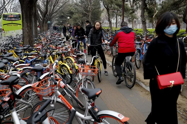 In this Thursday, March 23, 2017 photo, residents ride bicycles from bike-sharing company Ofo try to pedal through a sidewalk crowded with bicycles from the bike-sharing companies Ofo, Mobike and Bluegogo, near a bus stand in Beijing, China. (Photo by Andy Wong/AP Photo)