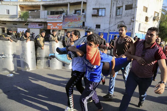 An injured protester is rushed to treatment as Iraqi security forces stand guard outside Baghdad's highly fortified Green Zone Friday, May 20, 2016. Iraqi security forces have fired tear gas and gunshots in the air as thousands of Shiite protesters stormed Baghdad's heavily secured Green Zone, rushing toward the prime minister's office and parliament building. (AP Photo/Karim Kadim)